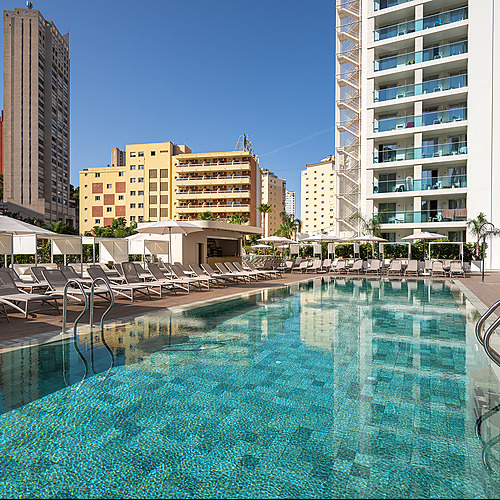 Piscina exterior del hotel con tumbonas, sombrillas y edificios modernos, perfecta para tu Port Hotels: Corporativa.