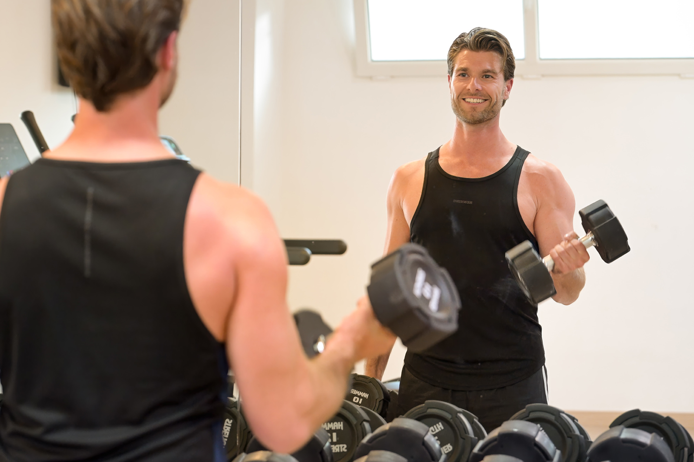 un hombre sostiene una mancuerna frente a un espejo en un gimnasio