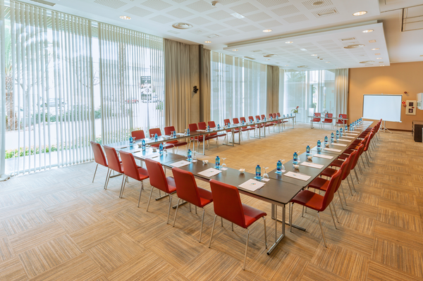 Una sala de conferencias moderna y vacía, con filas de sillas dispuestas hacia una pantalla de proyección.