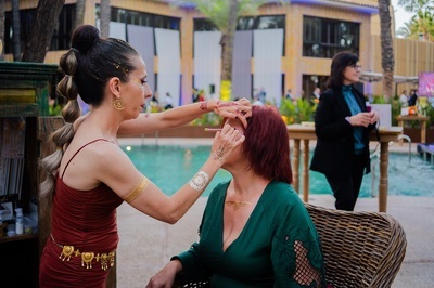 una mujer con un vestido rojo aplica maquillaje a una mujer con cabello rojo - 