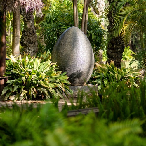a large stone egg is in the middle of a lush green garden