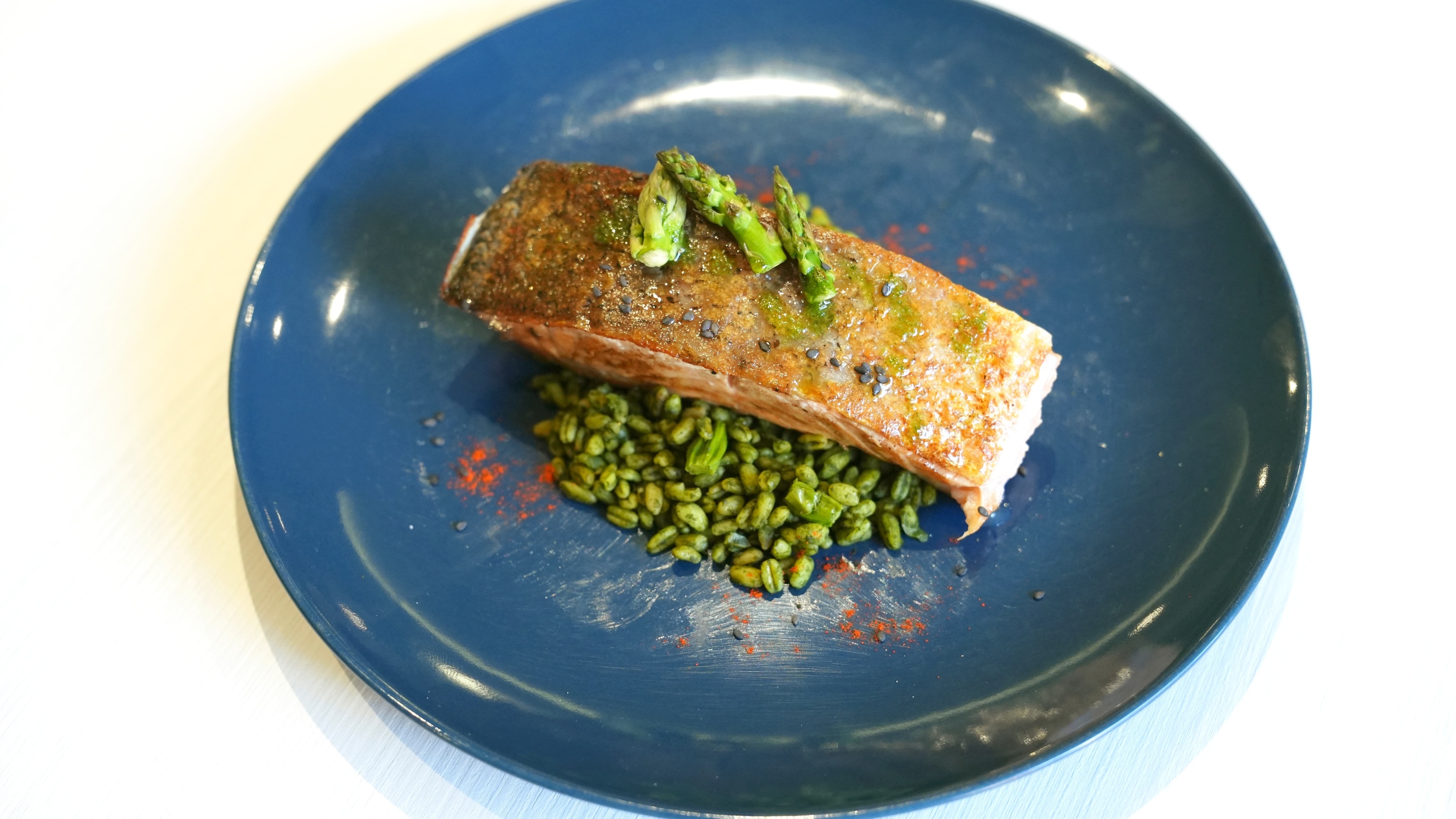 un plato azul con un trozo de pescado y espárragos encima