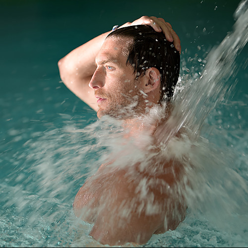 Hombre disfrutando de una cascada de agua en la piscina de un hotel. Port Hotels: Corporativa