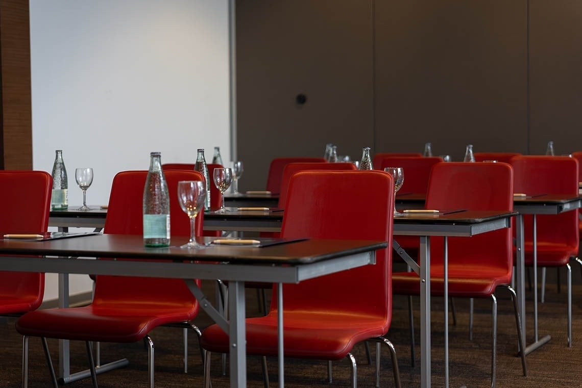 a row of tables with red chairs and bottles of water on them