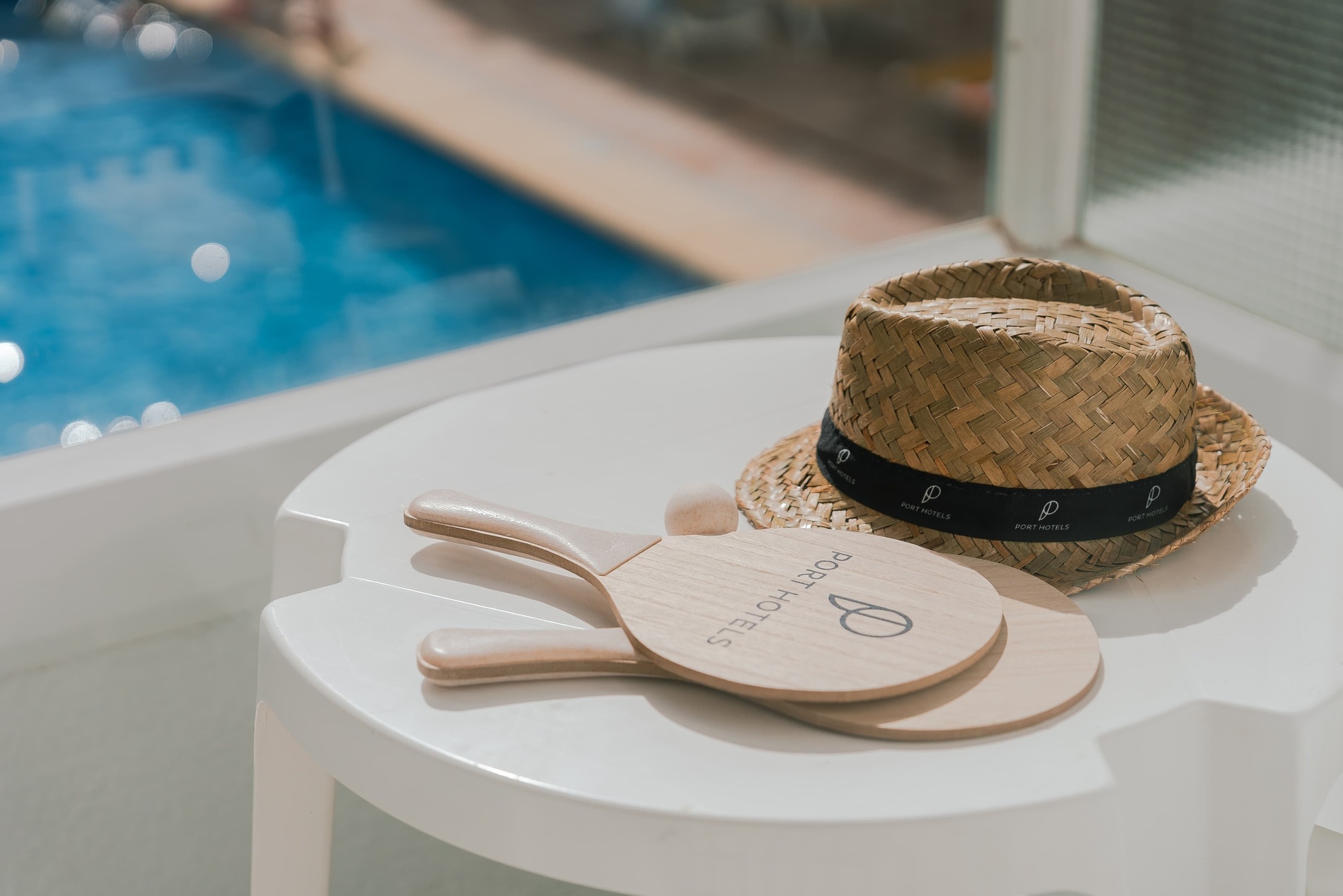 a straw hat sits on a white table next to a pair of rackets that say porthotel