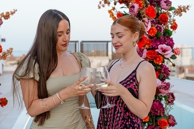 two women toasting with wine glasses in front of flowers - 