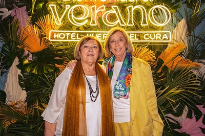 two women pose in front of a neon sign that says verano - 