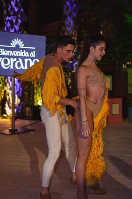 a man helps a woman dance in front of a sign that says bienvenido al verano - 