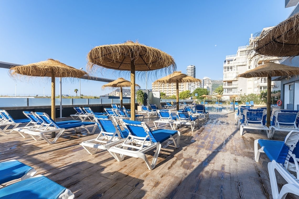 a swimming pool with blue chairs and a mountain in the background