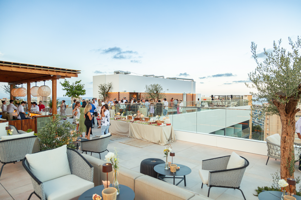 Un sendero serpentea a través de un exuberante entorno tropical con palmeras, césped verde y bungalows con tejados, bajo un cielo soleado.