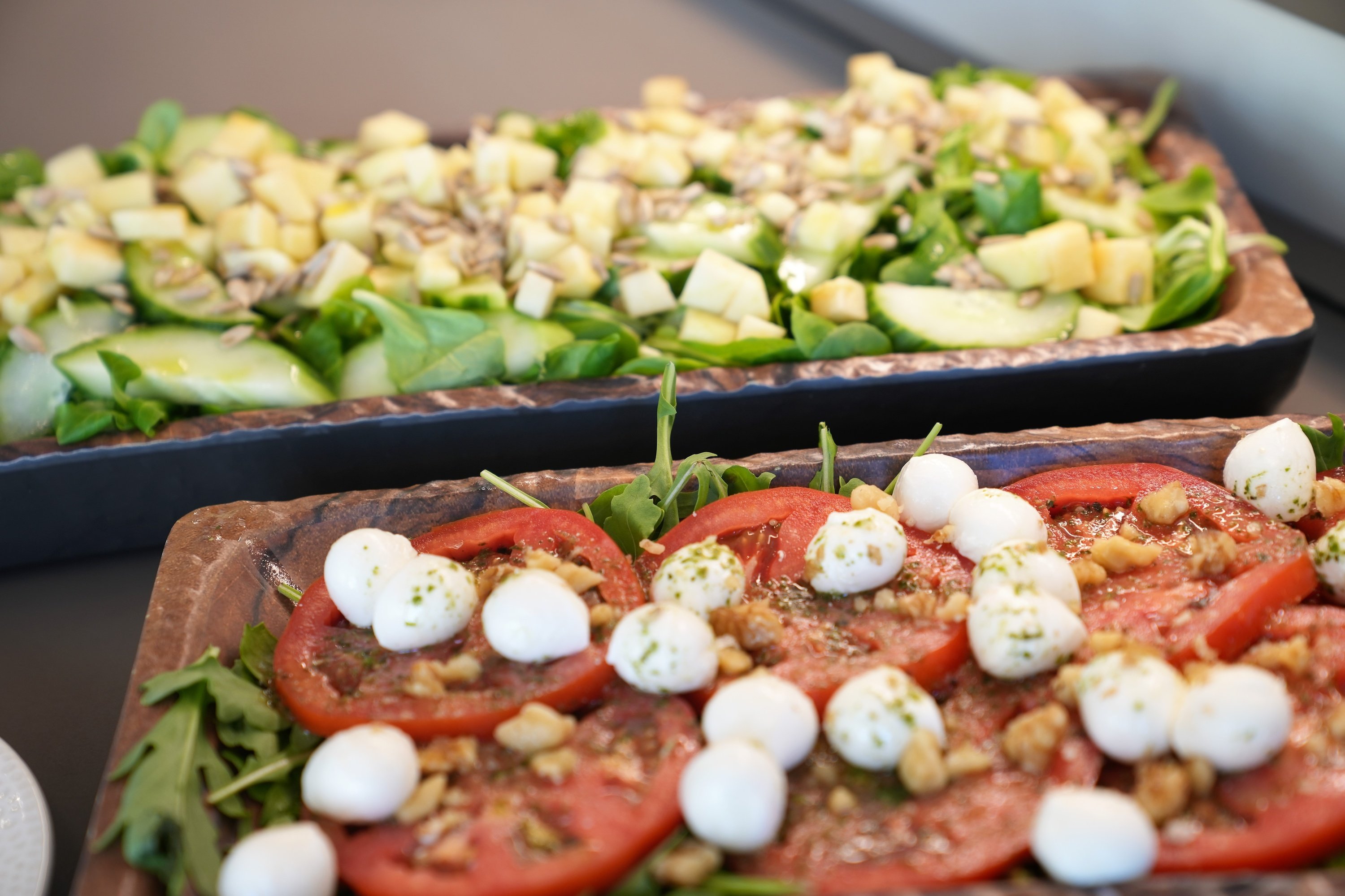 two trays of salads with tomatoes and mozzarella on them