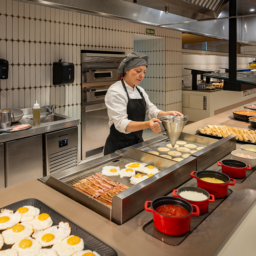 una mujer prepara huevos fritos y panqueques en una cocina
