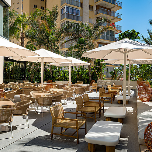 Terraza de hotel con sillas de ratán, mesas y sombrillas. Port Hotels: Corporativa.