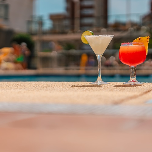 two drinks are on the edge of a swimming pool