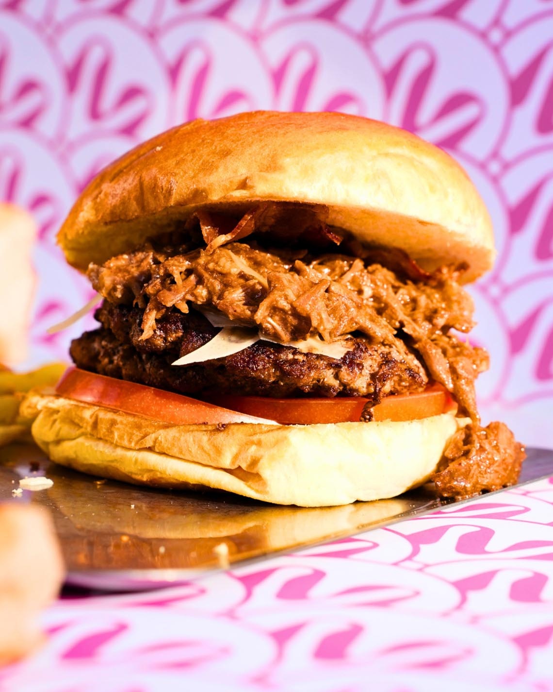 Burger gourmand avec fond rose abstrait, idéal pour les pauses gourmandes des événements Port Hotels: Corporativa.