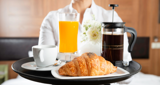 una mujer sostiene una bandeja de desayuno con un croissant y un vaso de jugo de naranja