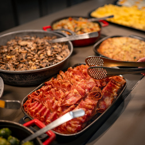 una persona sostiene pinzas sobre una bandeja de tocino