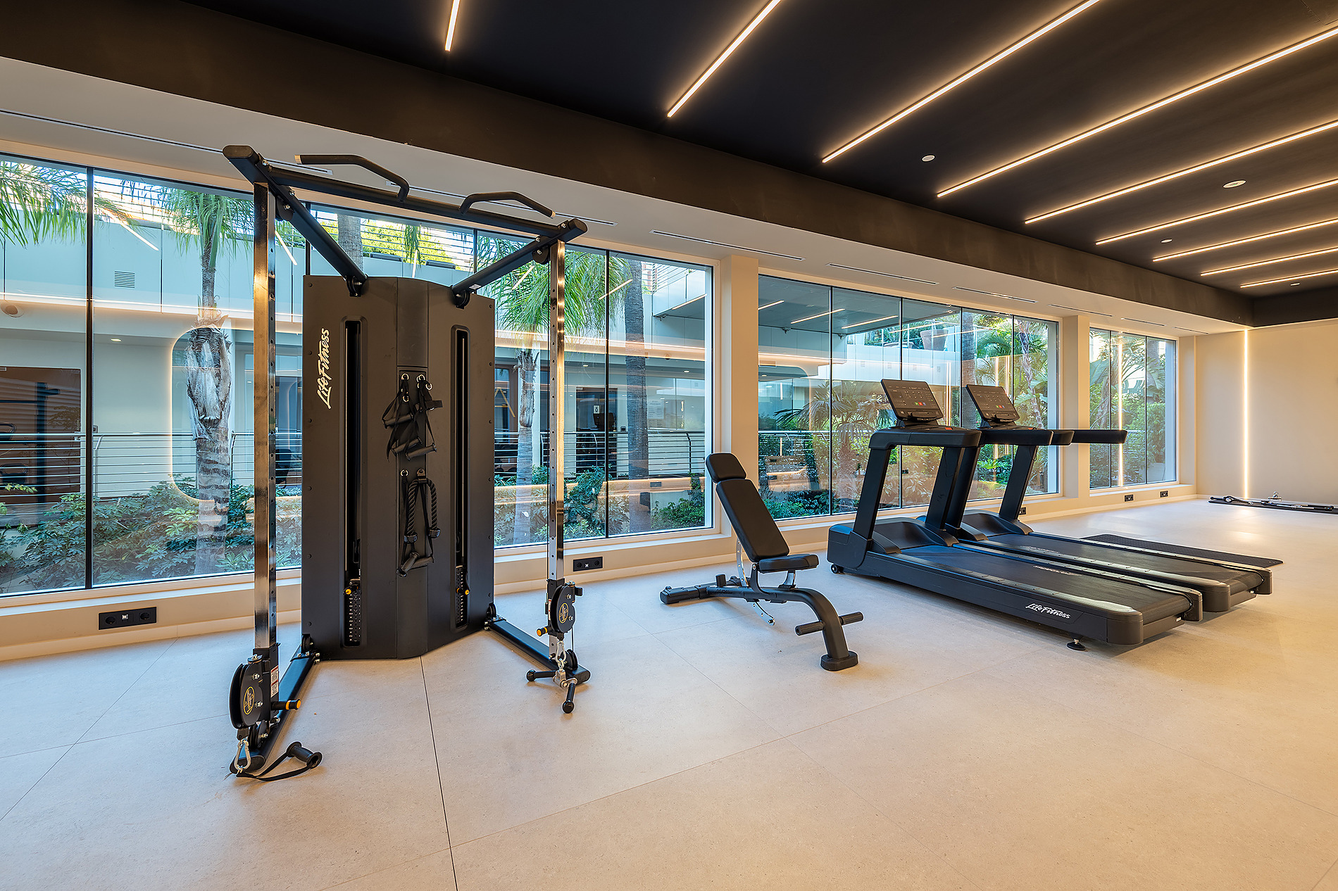 Gimnasio moderno con equipo Life Fitness, cintas de correr y banco, junto a ventanales con vistas al exterior. Ideal para el Bienestar Port Benidorm Hotel & Spa | Port Hotels | Web Oficial.