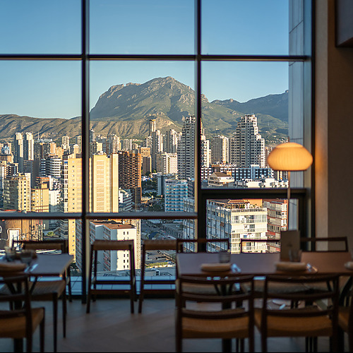Vista dePort Hotels: Corporativa desde el restaurante con mesas y sillas frente a una cadena montañosa y edificios.