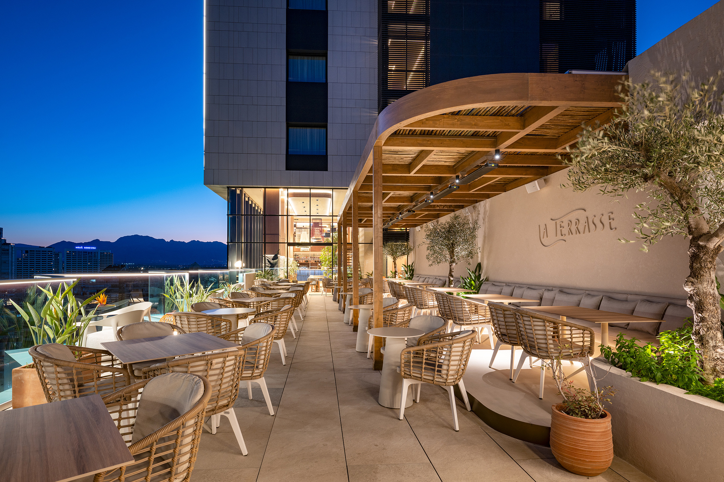 Terraza de hotel al anochecer con mesas y sillas de ratán, perfecta paraPort Hotels: Corporativa.