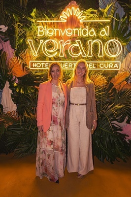 two women stand in front of a sign that says bienvenido al verano - 