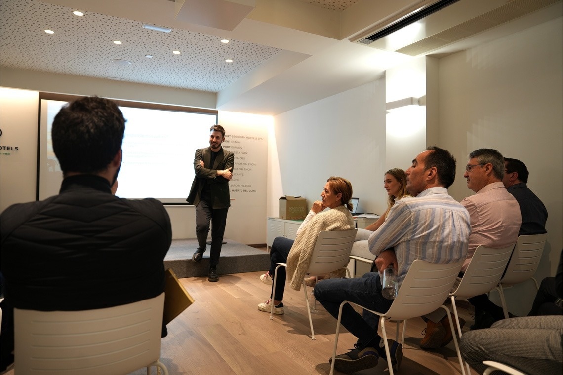 a man stands on a stage giving a presentation in front of a sign that says hotels