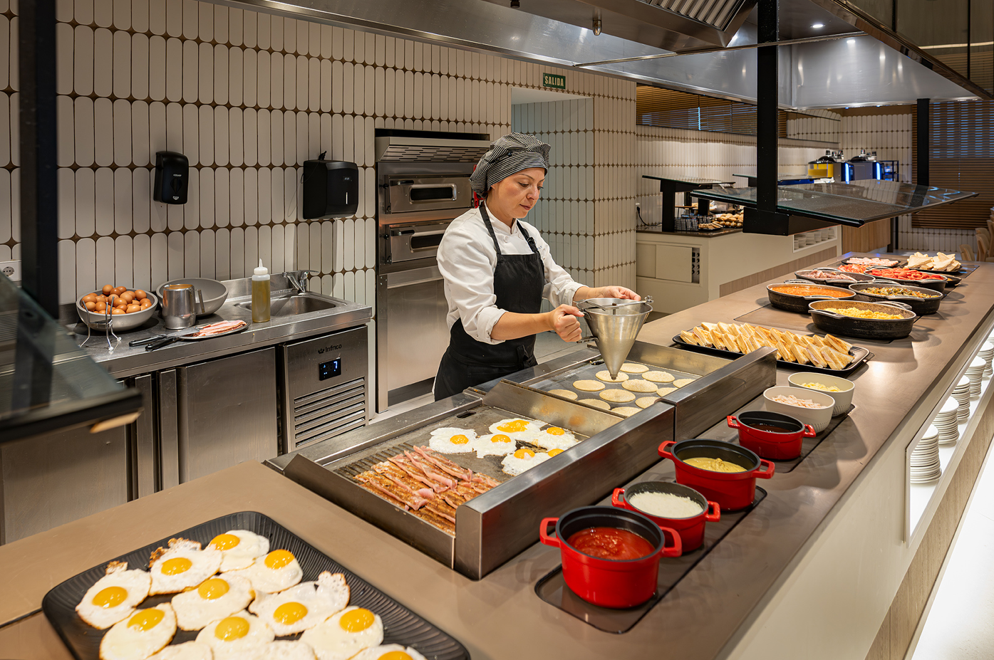 a woman is preparing food in a kitchen with eggs bacon and pancakes