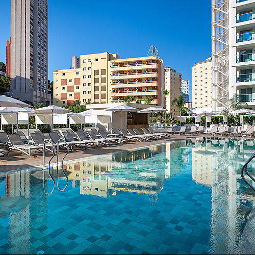 Piscina de hotel con tumbonas y edificios modernos, ideal para unas vacaciones Port Hotels: Corporativa.