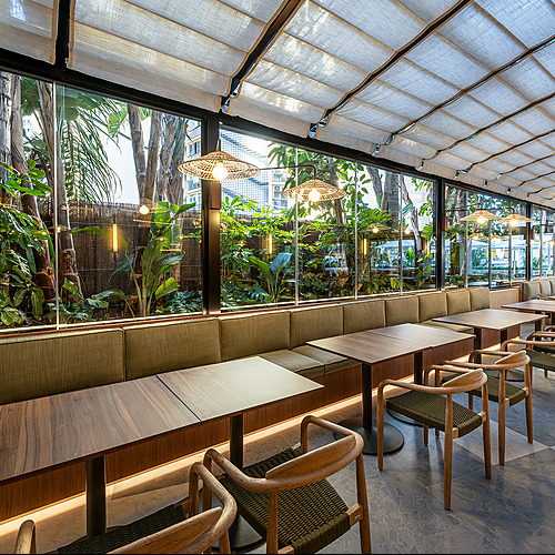 Interior de restaurante de hotel con mesas, sillas de madera y gran planta, vista a jardín exuberante. Port Hotels: Corporativa
