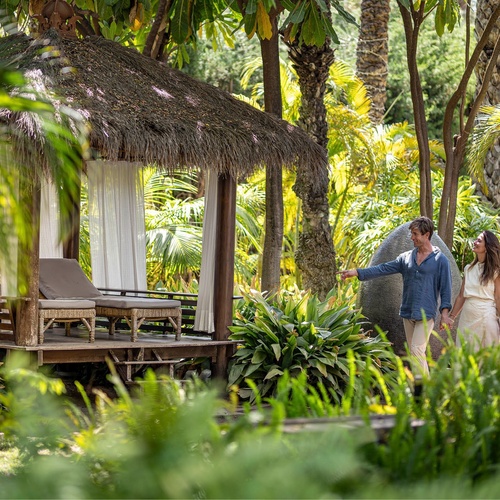 a man and woman holding hands in front of a hut