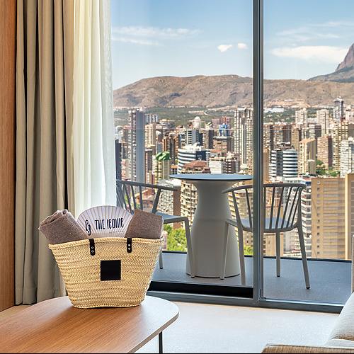 Hermosa vista de la ciudad y la montaña desde la habitación, con un bolso de playa y toallas en la mesa. Port Hotels: Corporativa