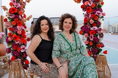 two women sitting next to each other in front of flowers - 