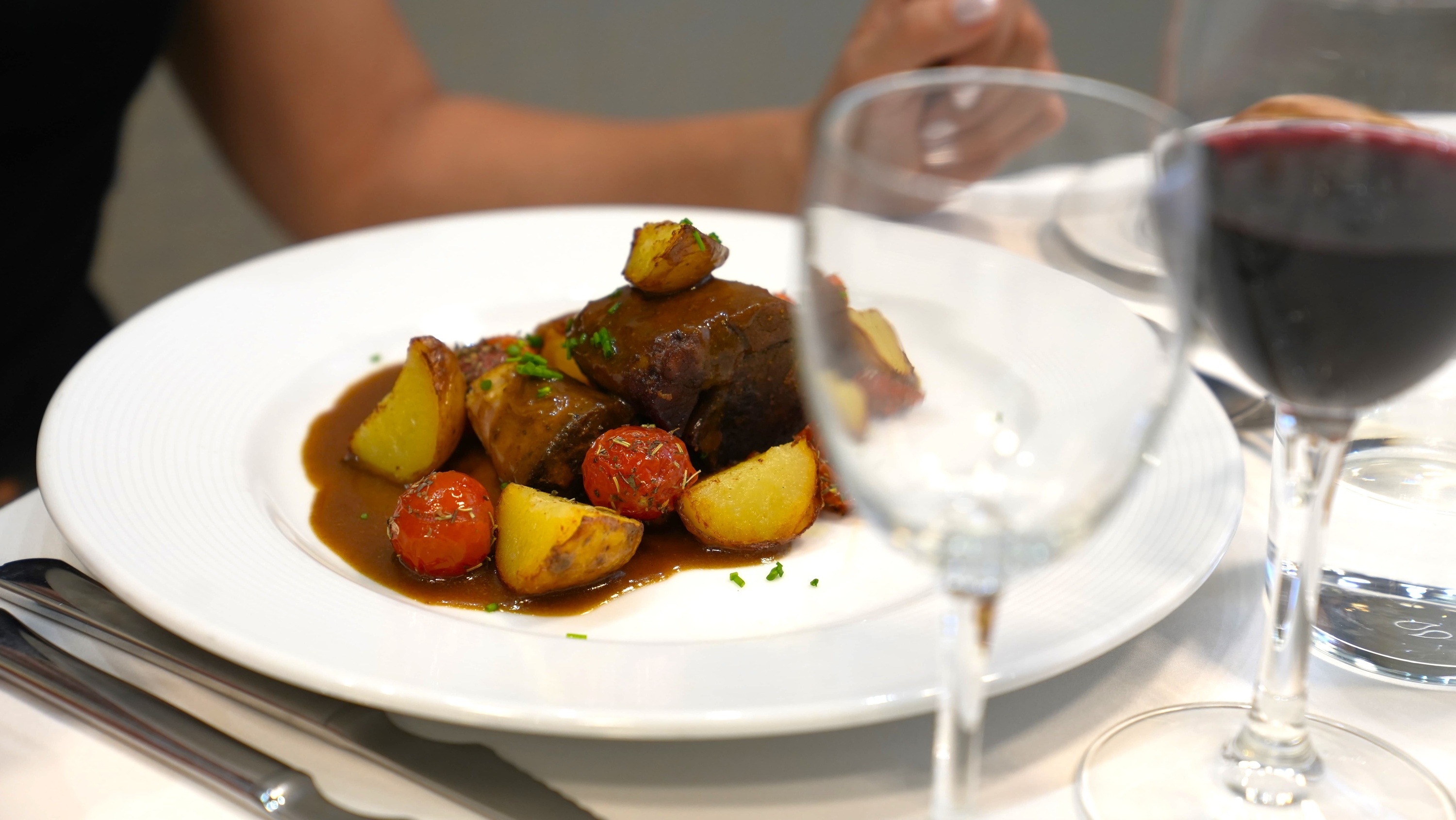 a plate of food with potatoes and tomatoes next to a glass of wine
