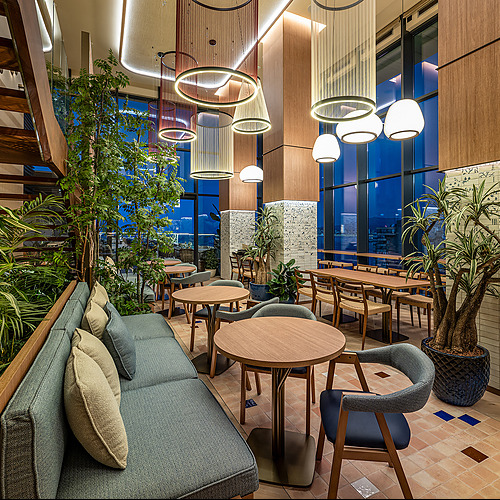 Elegante sala de estar de hotel con sofás azules, mesas de madera, plantas y vista nocturna de la ciudad. Port Hotels: Corporativa