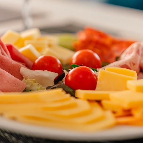 un plato blanco lleno de queso tomates y jamón