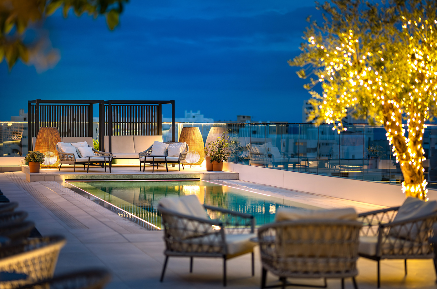una piscina rodeada de muebles y un árbol con luces amarillas
