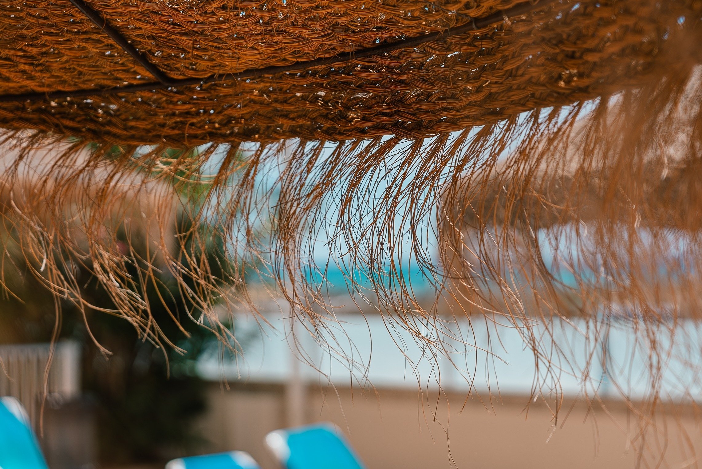 a close up of a straw umbrella with blue chairs in the background