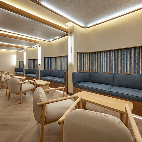 Sala de espera moderna con sofás azules, sillas beige, mesas de madera clara y iluminación ambiental. Port Hotels: Corporativa