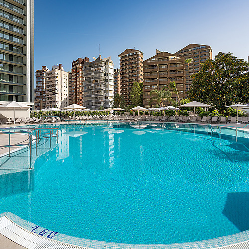 Piscina turquesa con tumbonas y edificios en el fondo, perfecta para Port Hotels: Corporativa.
