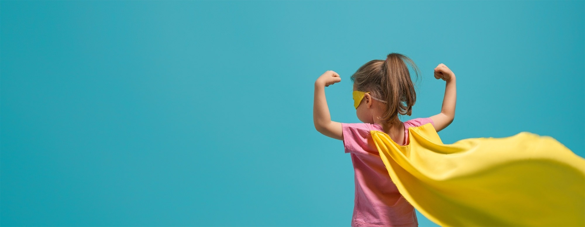  a little girl wearing a pink shirt and a yellow cape is flexing her muscles