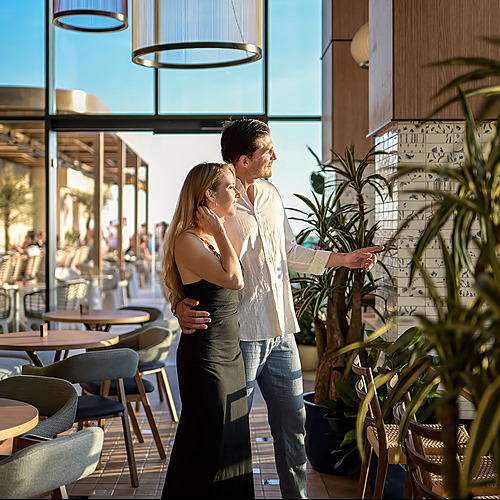 Pareja admirando la vista desde el restaurante de Port Hotels: Corporativa con plantas y mesas al aire libre.