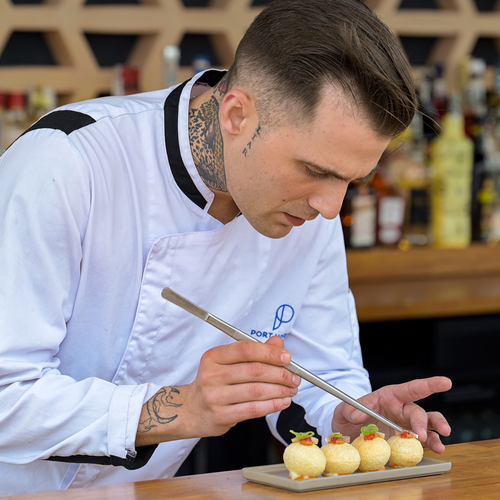 un chef con un tatuaje en la espalda decora un plato de comida