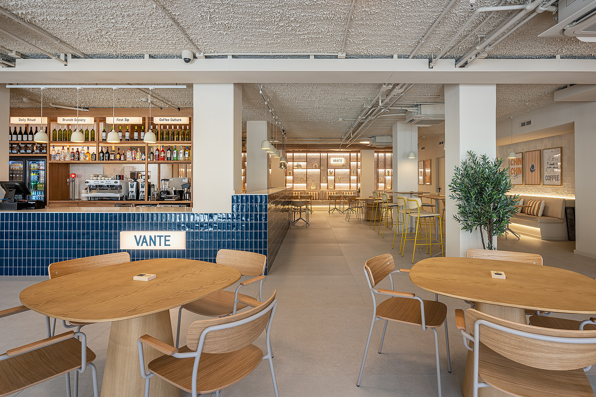 Interior de cafetería moderna con mesas de madera y sillas, barra de azulejos azules y letrero 'VANTE' Port Benidorm Hotel & Spa | Alicante | Port Hotels | Web oficial.