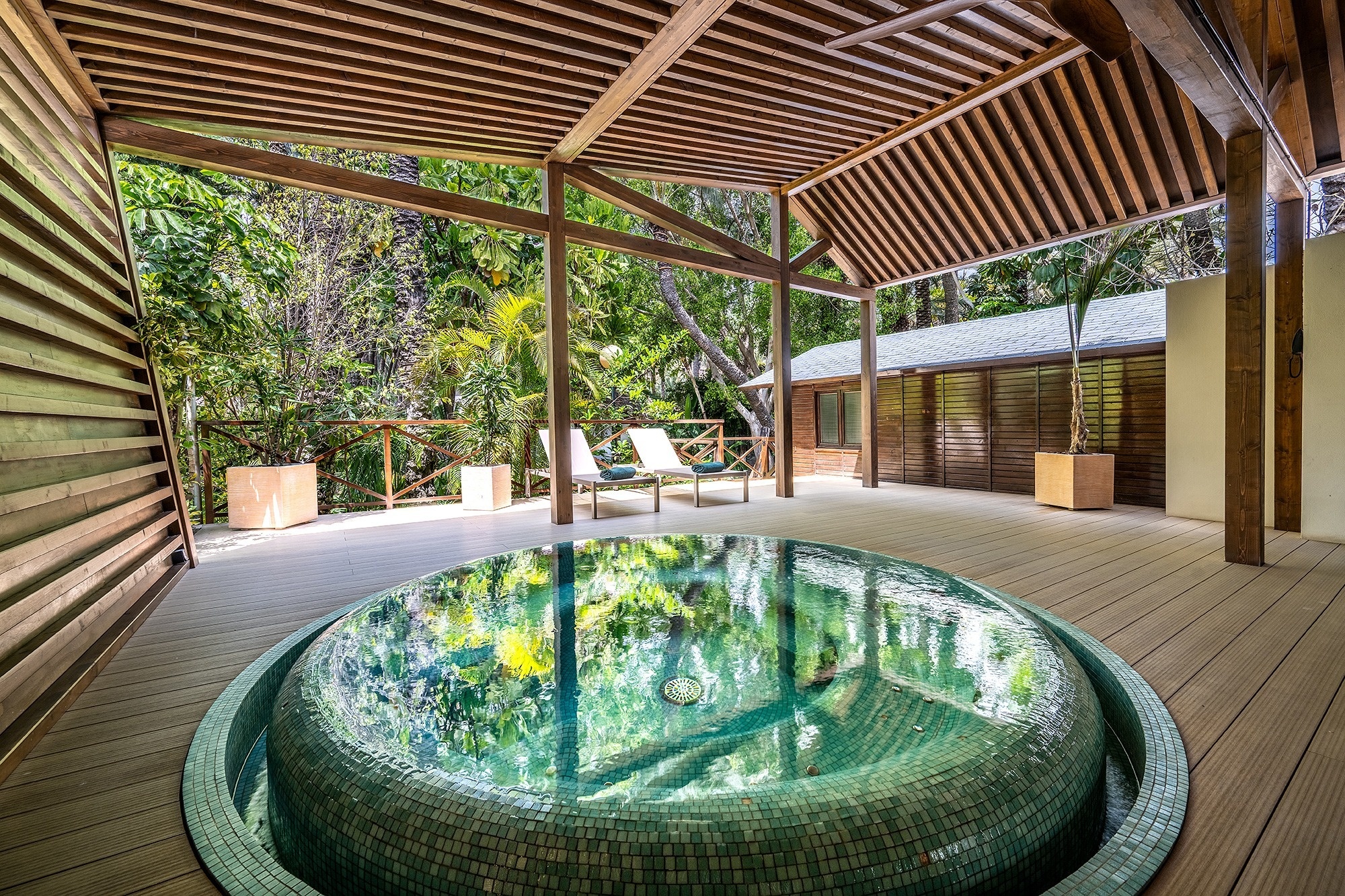 a hot tub is surrounded by lounge chairs under a wooden roof