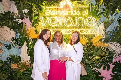 three women pose in front of a sign that says bienvenido al verano - 