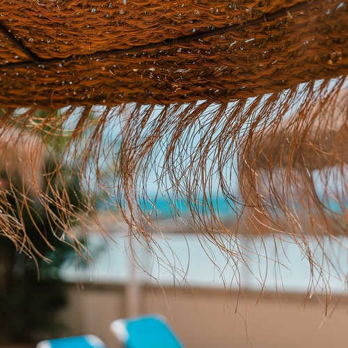 a close up of a straw umbrella with blue chairs in the background
