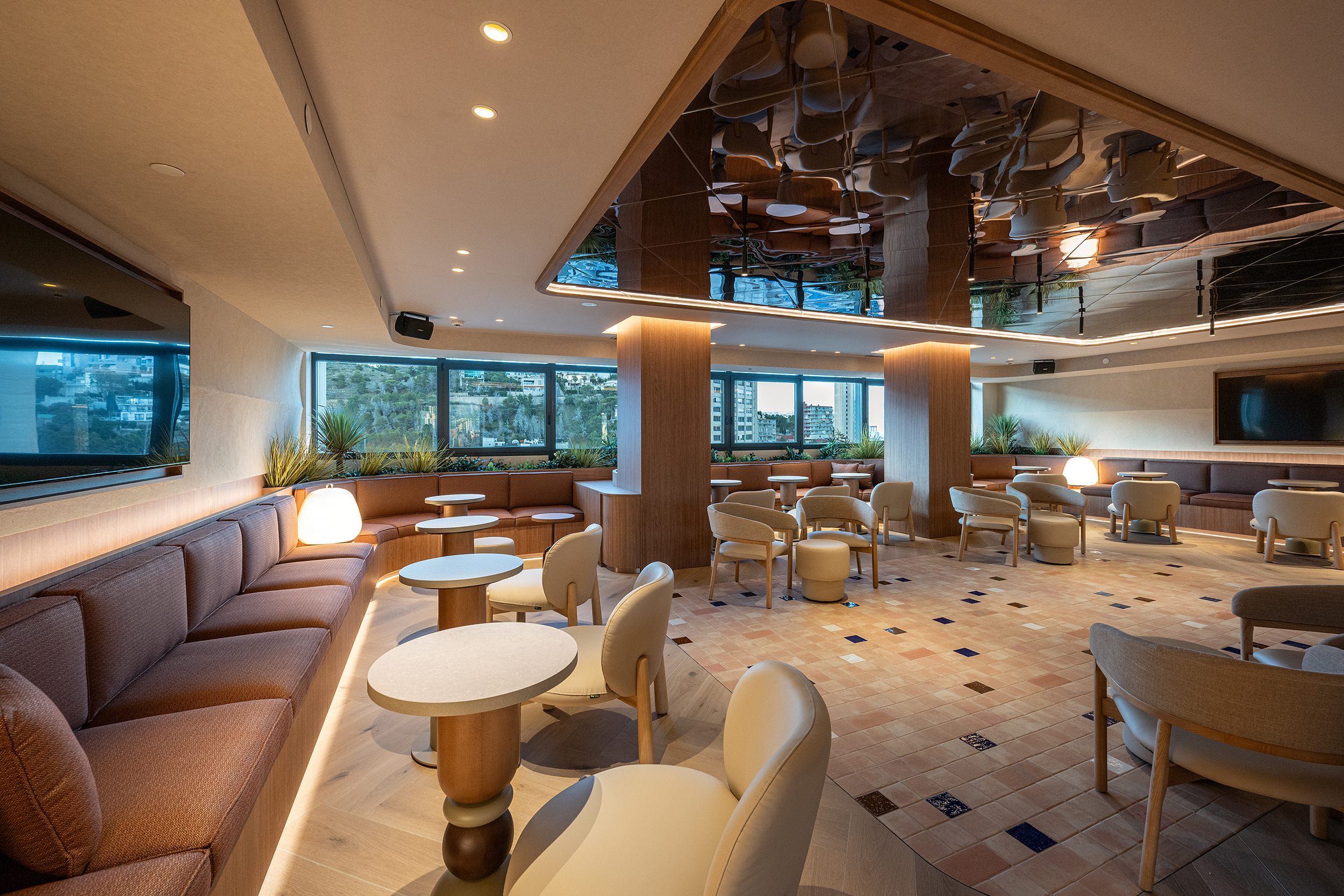 Salón moderno de hotel con sofás curvos, mesas circulares, sillas elegantes y techo espejado, ideal para Port Hotels: Corporativa.
