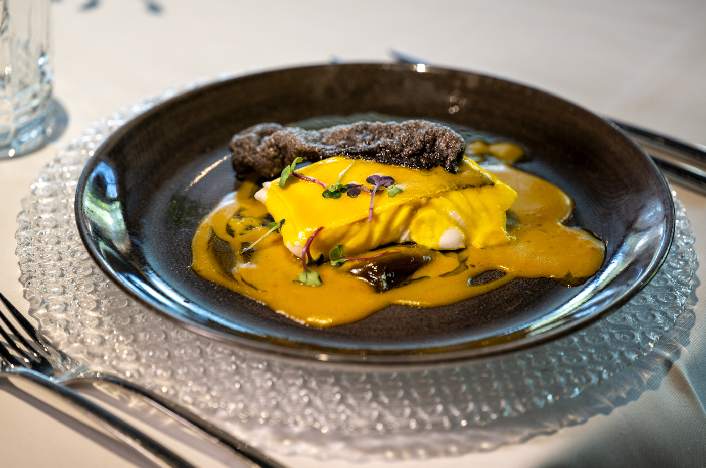 Gourmet fish entree with vibrant yellow sauce and unique garnish, beautifully plated for hotel fine dining.