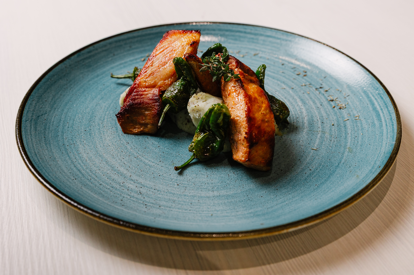 Crispy seared protein, green peppers, and mash on a blue plate, hotel restaurant dining.