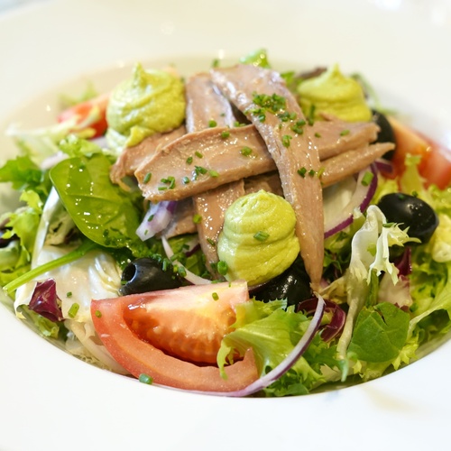 a salad with anchovies olives and tomatoes on a white plate